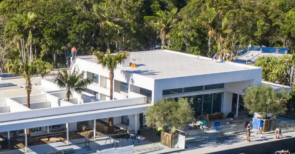 Aerial view of Chris Hemsworth House in Byron Bay, showcasing its modern architecture, lush palm trees, and expansive outdoor living spaces.