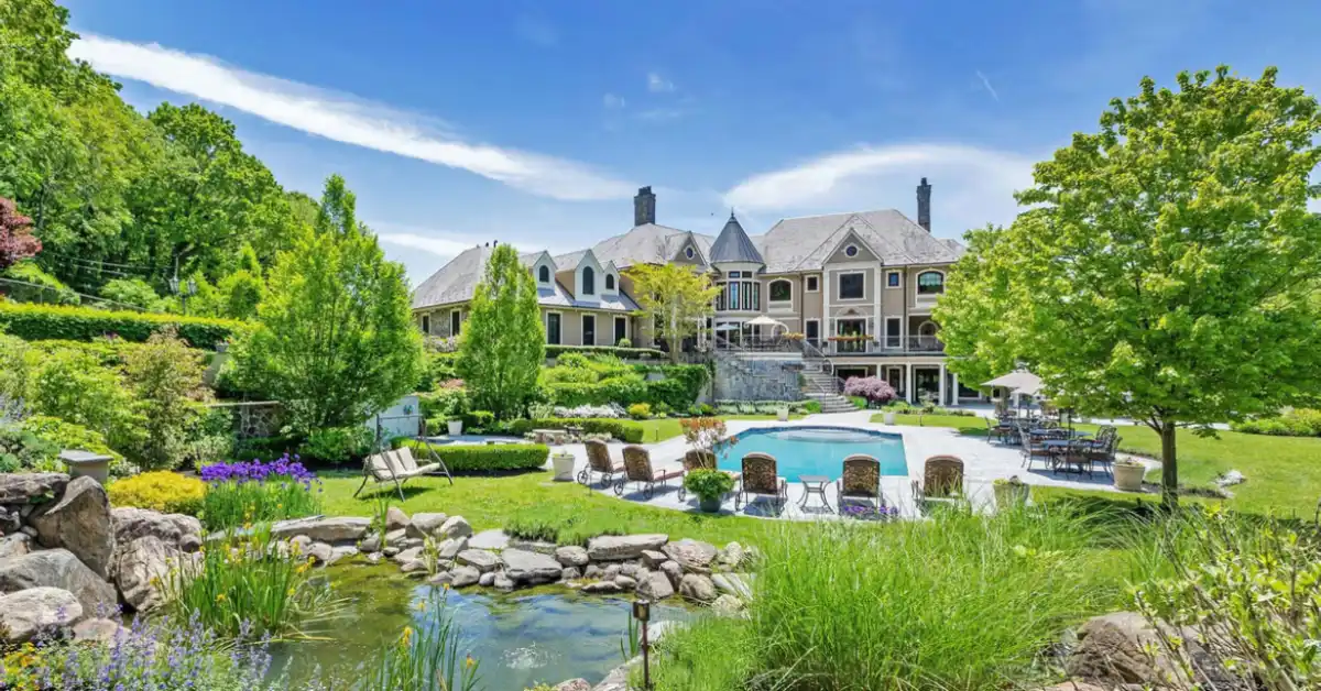 The Jordan Belfort House showcases a grand mansion with lush gardens, a sparkling pool, and elegant architecture, reflecting true luxury living.